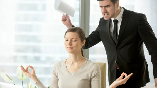 Businesswoman meditating calmly at desk as angry man in suit yells and waves paper behind her