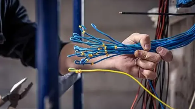 Electrician holding multiple blue network cables with yellow tags during wiring installation work.