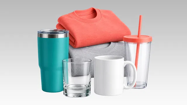 Teal insulated tumbler, empty glass, white coffee mug, coral and gray folded sweatshirts, clear tumbler with coral lid and straw.