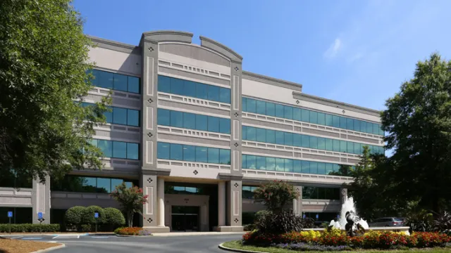Modern office building with large windows and landscaped roundabout fountain under clear blue sky