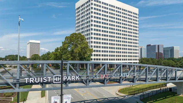 Truist Park sign on a metal pedestrian bridge with Atlanta office buildings and blue sky in the background