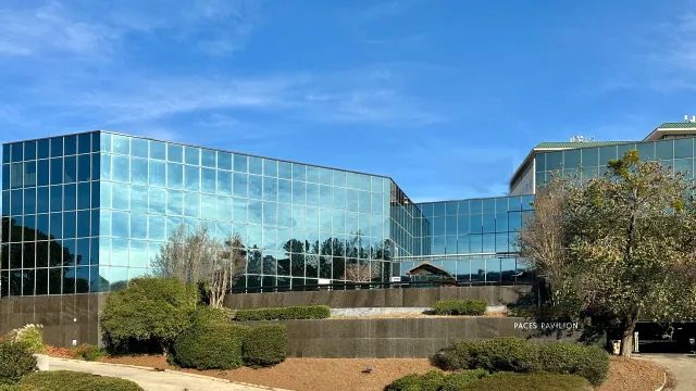 Modern glass office building reflecting sky and trees with landscaped shrubs and paved pathway