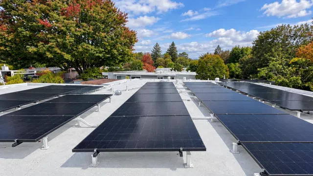 Rows of solar panels installed on a flat rooftop surrounded by trees with autumn foliage under a partly cloudy sky.