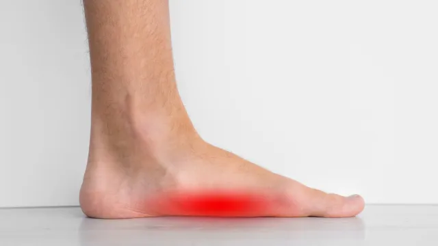 Side view of a bare foot with area of foot arch highlighted in red indicating pain or inflammation.