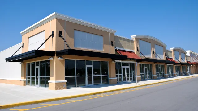 Empty modern retail shopping center with large glass windows under bright blue sky on a sunny day