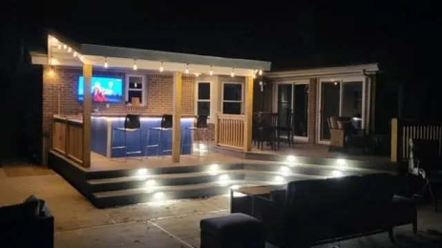 Outdoor patio bar and seating area illuminated at night with string lights and step lighting