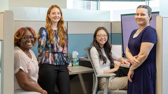 Diverse group of four professional women in office cubicle smiling and working together with computer