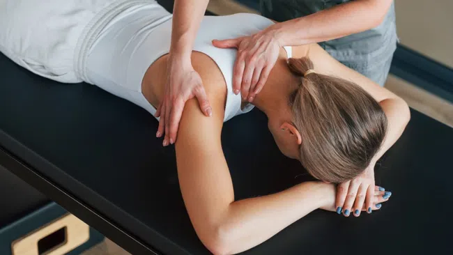 Woman receiving shoulder massage on a black therapy table in a wellness center.