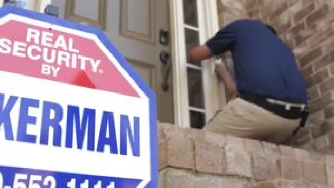 Technician installing a security system by the front door with a Kerman security sign in the foreground