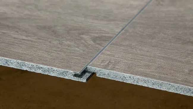 Close-up of two gray wood-textured interlocking laminate flooring panels showing their tongue and groove edges.
