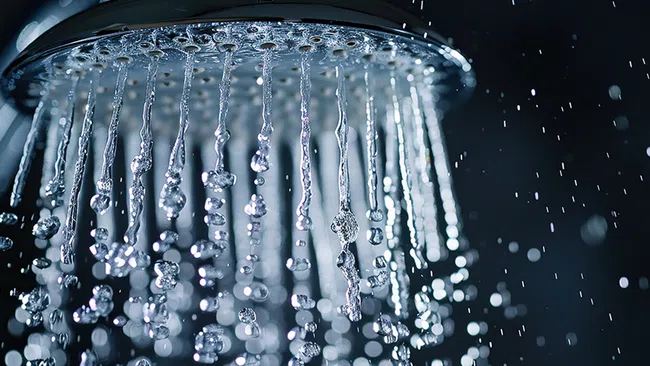 Close-up of water droplets flowing from a modern showerhead with dark blurred background and bokeh effects