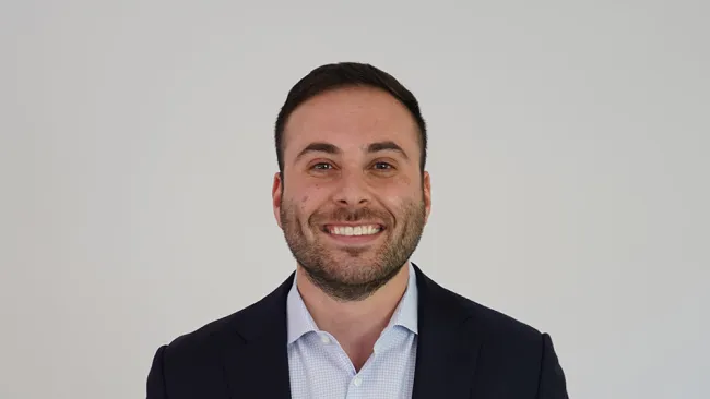 Professional man in a suit smiling against a plain background, showcasing a confident demeanor.