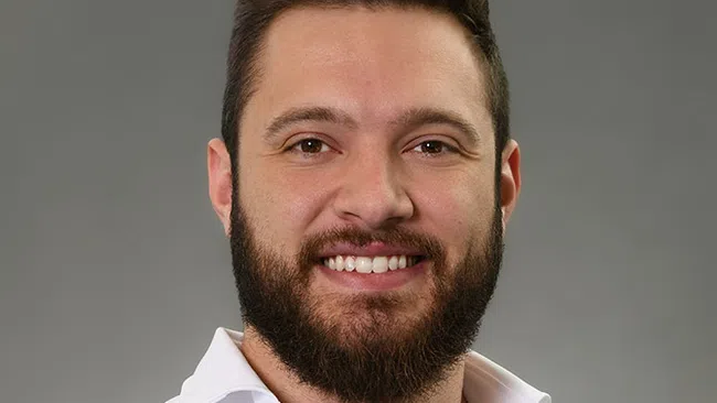 Smiling man with beard and styled hair wearing white dress shirt against gray background