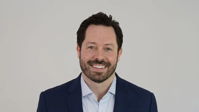 Smiling man in a blue suit against a neutral background, showcasing a professional appearance.