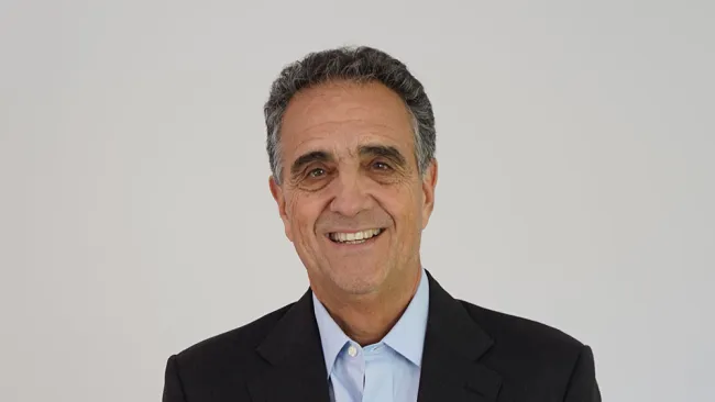Smiling man in a suit standing against a plain background, exuding confidence and approachability.