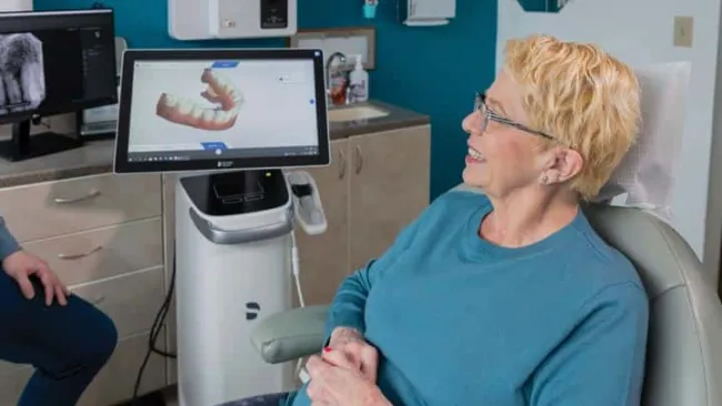 Senior woman smiling in a dental office with 3D digital dental model displayed on a computer screen