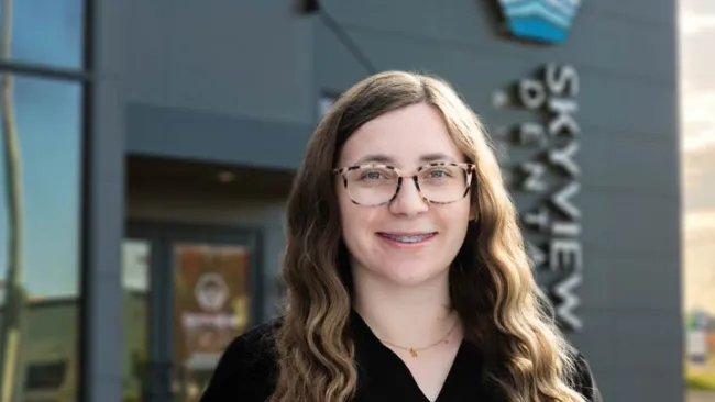 Smiling woman with glasses and long hair standing in front of Skyview Family Dental building exterior.