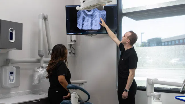Dentists examining a digital dental X-ray on a screen inside a modern dental clinic room.