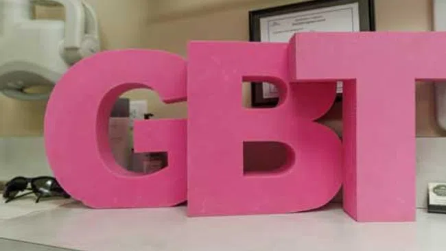 Large pink letters spelling GBT placed on a white countertop in indoor setting.