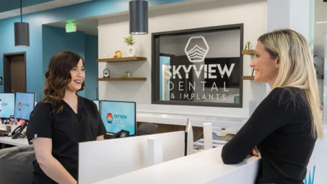 Dental receptionist assisting female patient at modern Skyview Dental office reception desk.