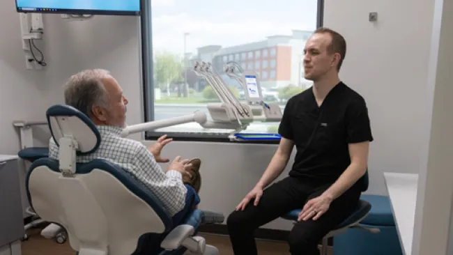 Dentist consulting with senior male patient in dental office with modern equipment and window view.