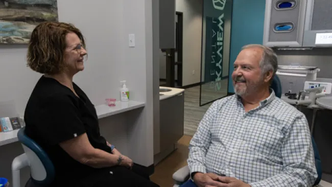 Dentist and patient smiling while sitting and talking in a modern dental clinic room.