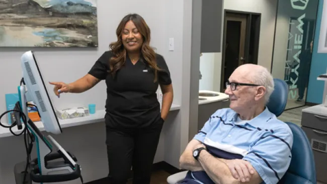 Healthcare worker in black scrubs showing information on a monitor to a seated elderly patient in a medical office