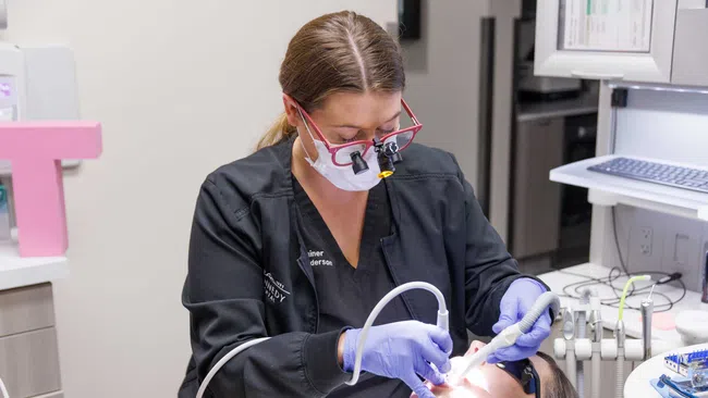 Dentist wearing magnifying glasses and gloves performing dental procedure on a patient in clinic