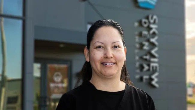 Smiling woman in black scrubs standing outside Skyview Dental clinic with sign in background.