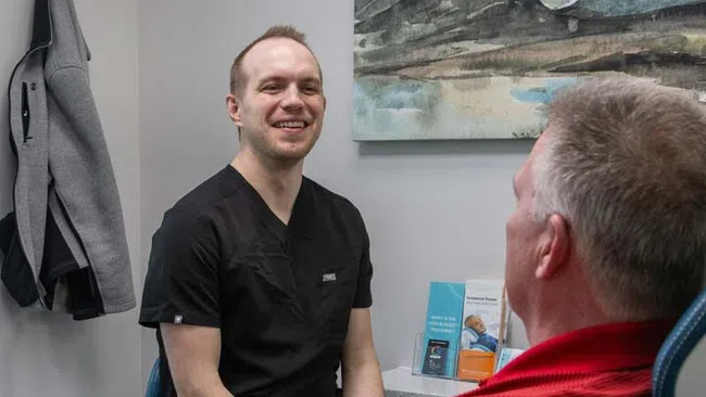 Dentist in black scrubs smiling and consulting with patient in red shirt in a modern dental office