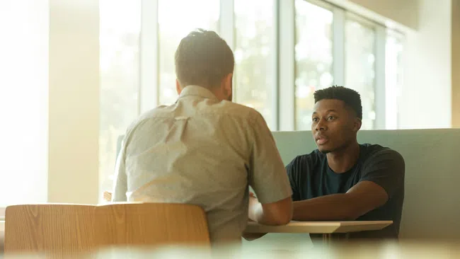 Two men sit at a table in a bright cafe having a focused conversation during the day.