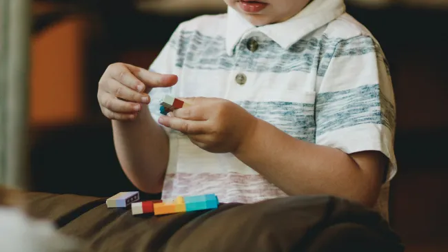 Child wearing striped shirt playing with colorful building blocks on a soft surface indoors