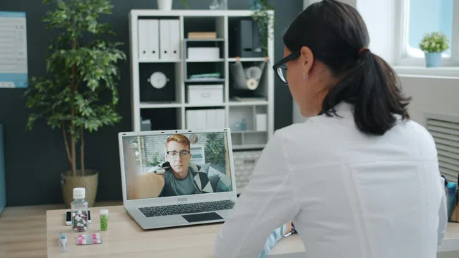 Doctor consulting a patient remotely via laptop video call in a modern office setting.