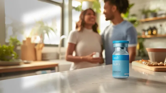 GLP-1 medication vial on kitchen countertop with a smiling couple in the background in a bright home setting
