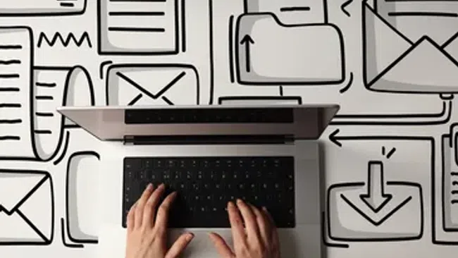 Hands typing on a laptop surrounded by digital email and file icons drawn on a white surface