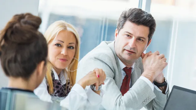 Three professionals engaged in a business meeting with laptop in a bright office setting