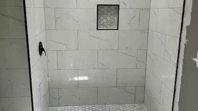 Modern walk-in shower with white marble tiles and hexagon floor tiles next to a white toilet.