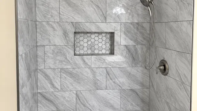 Modern shower with marble tile walls, hexagonal floor tiles, built-in shelf, bench, and handheld showerhead.