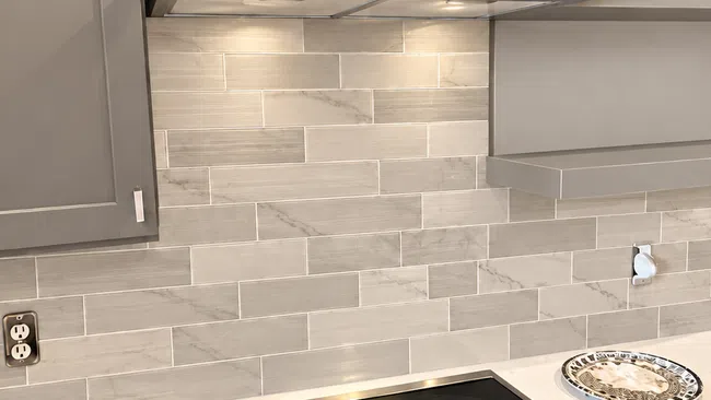 Modern kitchen stove with black glass cooktop, stainless steel range hood, and beige tiled backsplash.