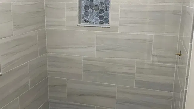 Modern shower with large rectangular beige wall tiles and hexagonal patterned blue-gray floor tiles with built-in niche.