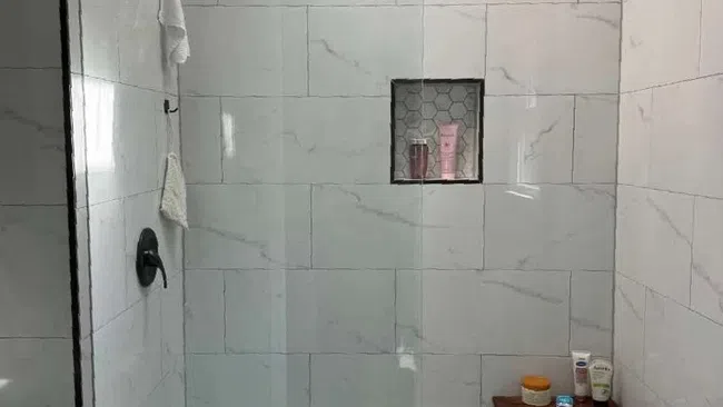 Modern walk-in shower with marble-effect tiles, hexagonal floor tiles, built-in shelf, and wooden corner bench.