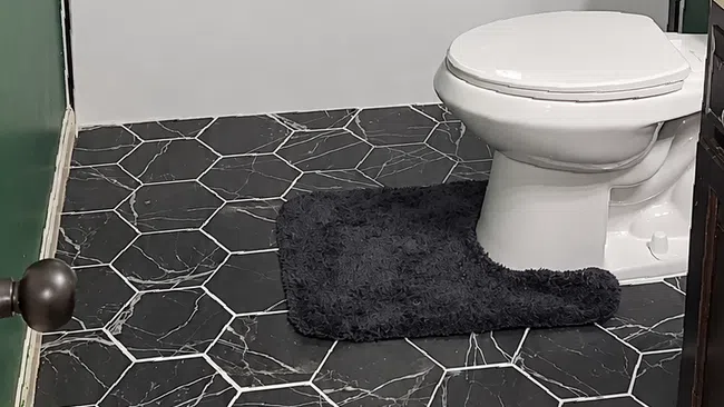 Modern bathroom with black hexagonal floor tiles, glass shower door, white toilet, and green walls.