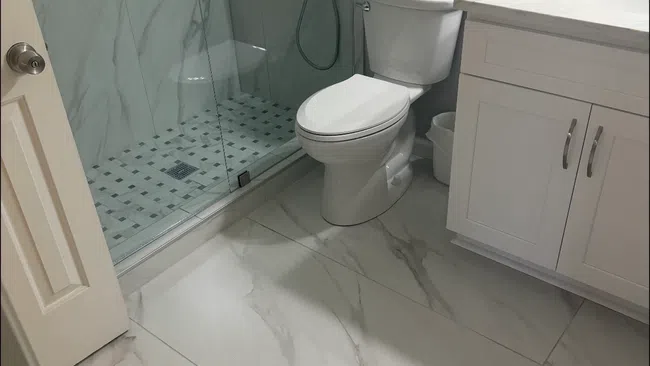 Modern bathroom with glass shower enclosure, white toilet, marble floor and white vanity with sink.