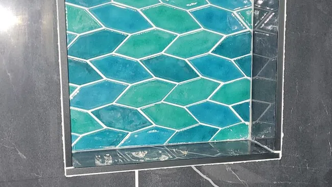 Niche with teal and blue geometric tiles set inside a black marble wall with white veins and grout.