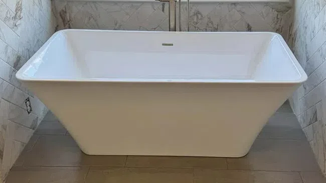 White freestanding bathtub with modern faucet under a large window overlooking a grassy yard.