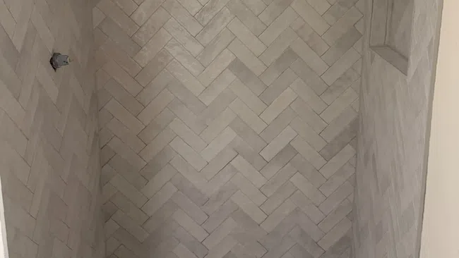 Walk-in shower with herringbone wall tiles and circular mosaic floor tiles in neutral tones.