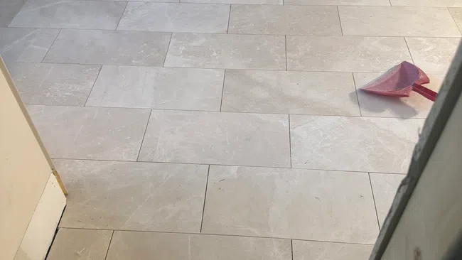 Light beige ceramic floor tiles freshly installed in a room under renovation with tools scattered around.