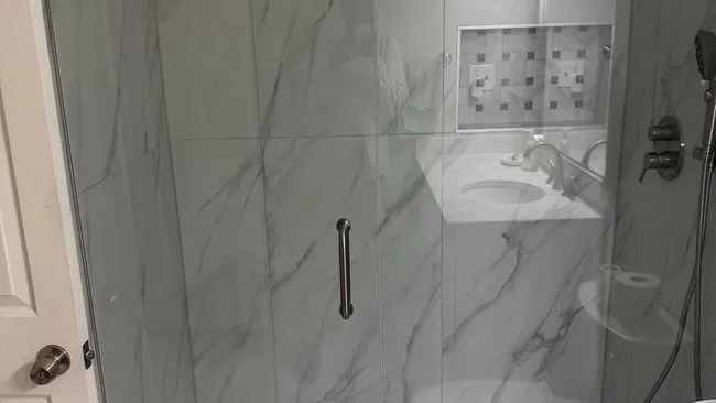 Modern bathroom with marble walls, a glass shower enclosure, tiled floor, and a white toilet.