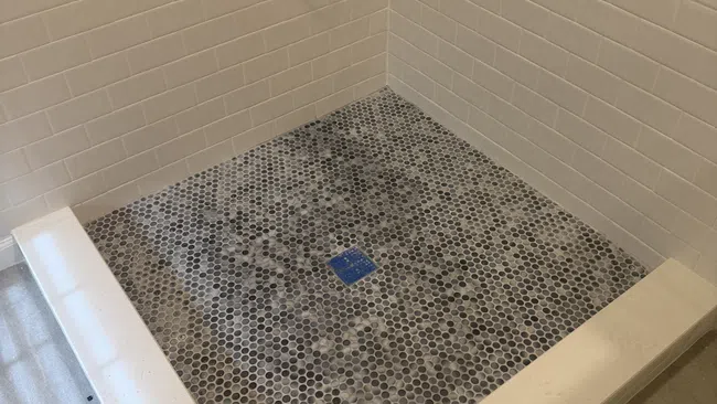 Bathroom shower with white subway tiles on walls and hexagonal mosaic tile flooring with a built-in drain.