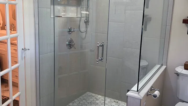 Modern glass shower enclosure with hexagonal tile floor and rain showerhead in a bright bathroom
